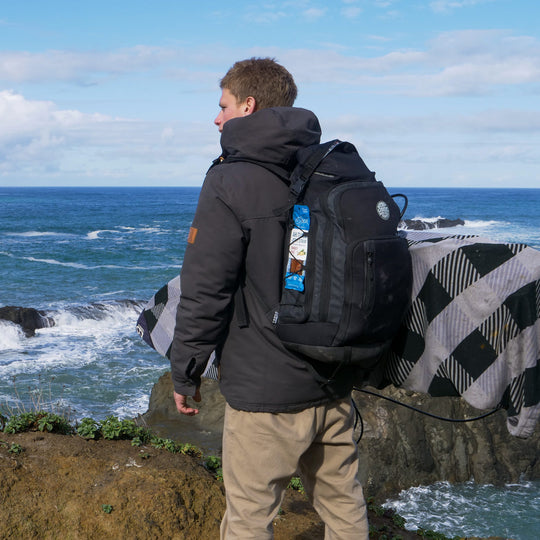 Man standing on a cliff near the ocean with Pescavore tuna in his backpack