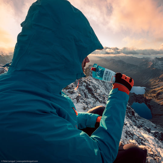 Hiker eating Pescavore tuna at sunrise in front of a backdrop of mountains